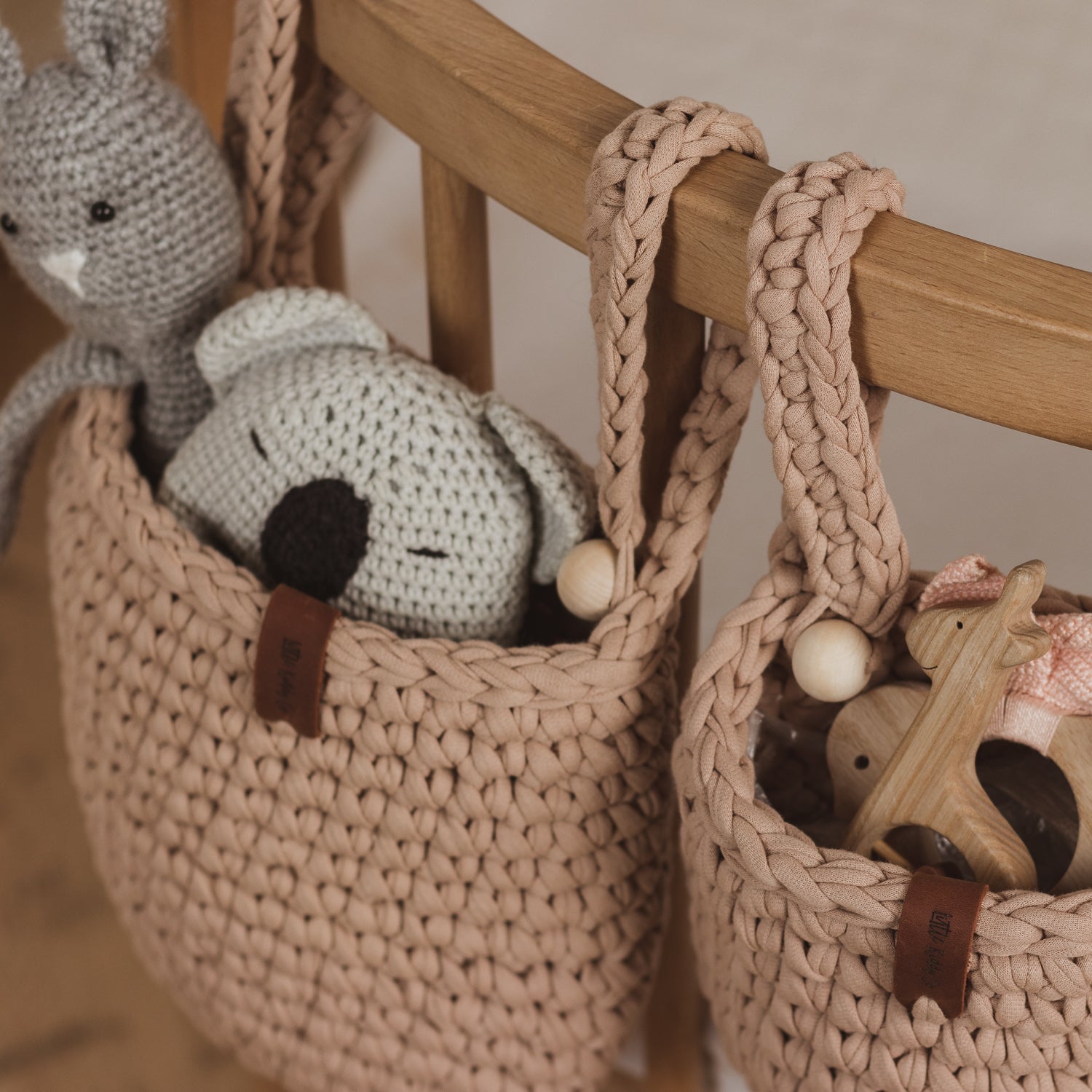Two crochet baskets with toys hanging on a wooden rack.