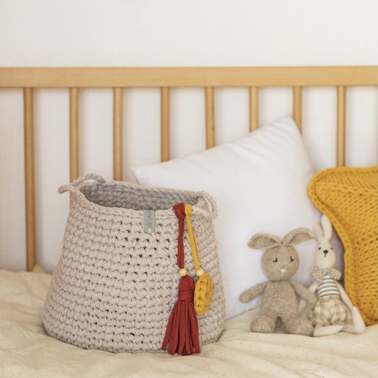 Woven basket with colorful tassels on a bed with plush toys and pillows.